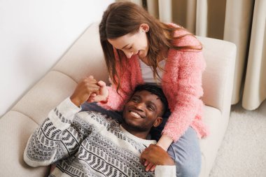 Gülümseyen kadın evdeki kanepede Afro-Amerikan erkek arkadaşının elini tutuyor.