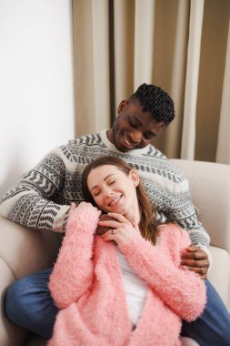 Mutlu Afro-Amerikalı adam evdeki kanepede kız arkadaşına sarılıyor.