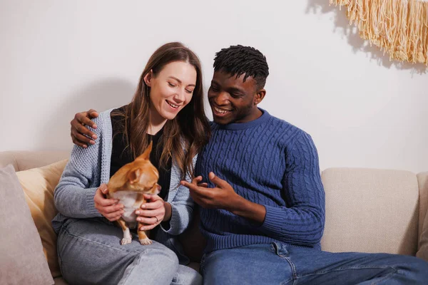 Gülümseyen ırklar arası bir çift evdeki kanepede evcil hayvanla vakit geçiriyor.