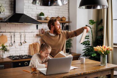 Sakallı baba kitap okuyarak kızını desteklerken bilgisayarın yanında bilgisayar ve mutfakta içki öğreniyor.