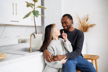 Kazaklı genç Asyalı kadın mutfakta gülümseyen Afrikalı Amerikalı erkek arkadaşla konuşuyor.