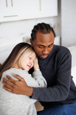 Genç Afrikalı Amerikalı adam mutfakta Asyalı kız arkadaşına sarılıyor.