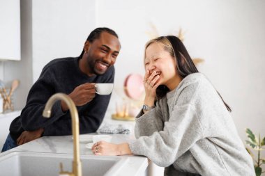 Kahvenin yanında gülen zarif Asyalı kadın ve mutfakta Afrikalı Amerikalı erkek arkadaş.