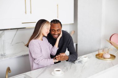 Gülümseyen Asyalı kadın, modern mutfakta kahvenin yanında Afro-Amerikan erkek arkadaşının elini tutuyor.