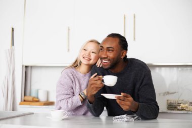 Gülümseyen Afrikalı Amerikalı adam mutfakta genç Asyalı kız arkadaşının yanında kahve tutuyor.
