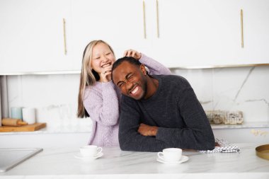 Gülümseyen Asyalı kadın. Afro-Amerikan erkek arkadaşının saçlarına dokunuyor. Mutfakta kahvenin yanında.