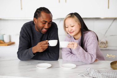 Gülümseyen genç bir çift sabah mutfakta kahve fincanları tutuyorlar.