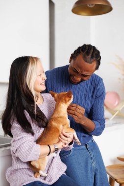 Evde Afro-Amerikan erkek arkadaşının yanında elinde Chihuahua köpeği tutan pozitif Asyalı bir kadın var.