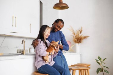 Chihuahua köpeği tutan ve mutfakta kucaklaşan pozitif, genç bir çift.