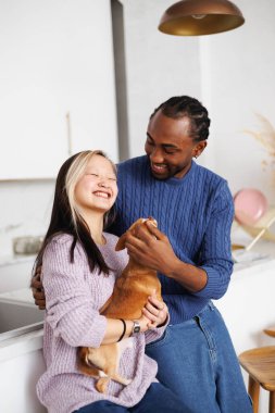 Modern mutfakta, Afrikalı Amerikalı erkek arkadaşın yanında elinde chihuahua köpeği tutan neşeli Asyalı genç kadın.