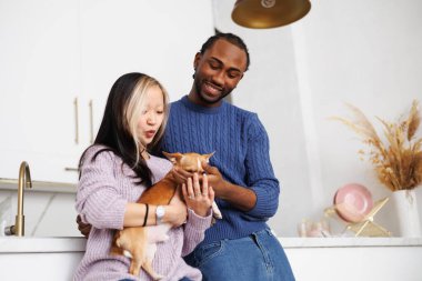 Modern mutfakta süveter giyen, Chihuahua köpeği tutan ırklar arası genç bir çift.