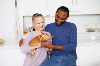 Gülümseyen Afro-Amerikan adam Asyalı kız arkadaşına sarılıyor evde Chihuahua köpeğiyle