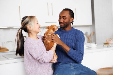 Gülümseyen Asyalı kadın, mutfakta Afrikalı Amerikalı erkek arkadaşına chihuahua sosisi veriyor.