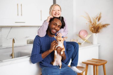 Kameraya gülümseyen ve evde Chihuahua köpeği tutan çok ırklı bir çift.