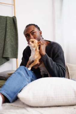 Eşofmanlı genç Afro-Amerikan adam evdeki evcil hayvan yatağıyla rahatlıyor.