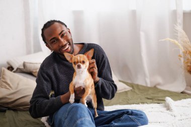 Neşeli, Afro-Amerikalı Amerikalı bir adam evdeki yatakta kameraya bakıyor.