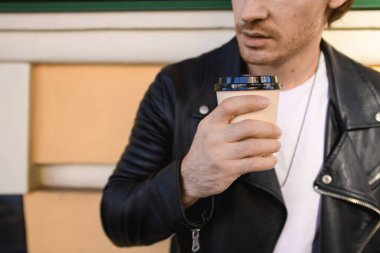 Deri ceketli bir adamın tek kullanımlık bardakta kahve taşıdığı görüntüler.