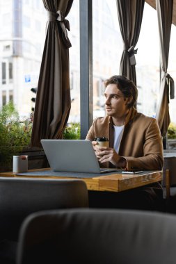 Cafe 'deki masalara yakın oturmak için elinde kahve tutan şık bir işadamı.