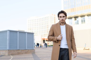 Kahverengi saçlı adam şehirdeki kameraya bakıyor.