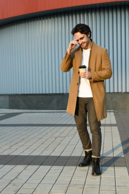 Paltolu ve botlu mutlu adam şehir sokaklarında yürürken bir şeyler içer.