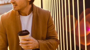 Gün batımında elinde kağıt bardakla gülümseyen adam görüntüsü.