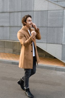 Mutlu iş adamı akıllı telefonla konuşurken ve şehir caddesinde yürürken evet işareti yapıyor.