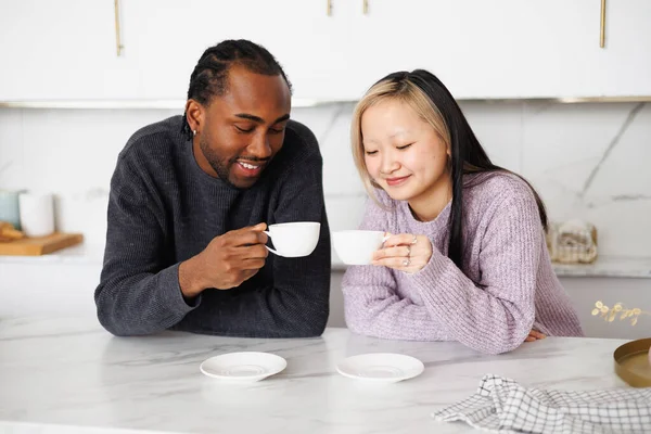 Gülümseyen genç bir çift sabah mutfakta kahve fincanları tutuyorlar.