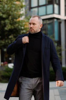 Sonbaharda şehir caddesinde yürüyen montlu bir işadamı.