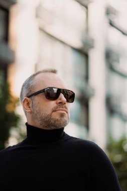 Şehir caddesinde duran güneş gözlüklü ve balıkçı yakalı zarif bir adamın portresi.