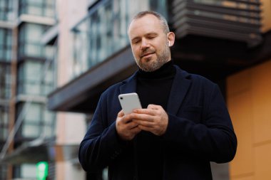 Şehir caddesinde akıllı telefon ve kulaklık kullanan palto giyen bir işadamı.