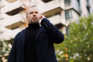 Sonbaharda şehir caddesinde şık kıyafetler içinde akıllı telefon kullanan yetişkin bir adam.