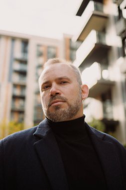 Sonbaharda şehir caddesinde kameraya bakan montlu yetişkin bir adamın portresi.