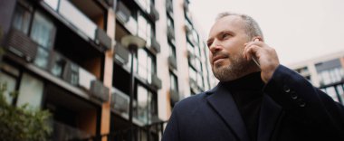 Sonbaharda kentsel caddede dizüstü bilgisayar kullanan palto giymiş yetişkin işadamı, afiş