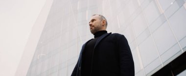 Ofis binasının yanında duran paltolu yetişkin işadamının düşük açılı görüntüsü, afiş.