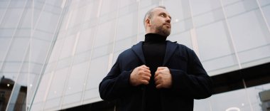 Caddedeki ofis binasının yanında paltolu işadamının alçak açılı görüntüsü, afiş.