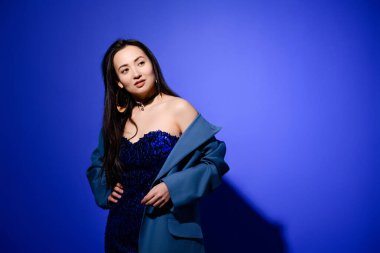 Mavi arka planda poz veren şık Asyalı kadın.