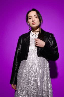 Payet ve deri ceketli modaya uygun genç Asyalı kadın mor üzerinde duruyor.