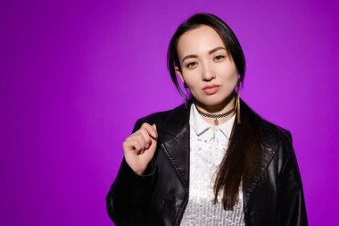 Mor üzerine izole edilmiş deri ceketli kendine güvenen ve şık Asyalı bir kadının portresi.