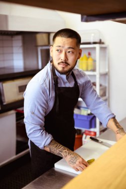 Önlüklü Asyalı şef kafedeki salatalıkların yanından uzağa bakıyor.