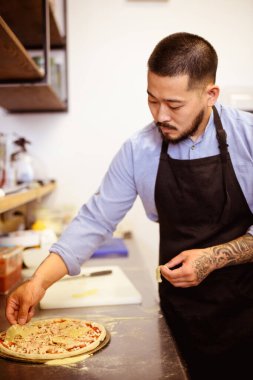 Asyalı şef, kafede yemek pişirirken çiğ pizzaya ananas koyuyor.