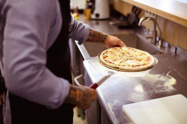 Yüzü olmayan aşçı kafedeki küreklere pizza koyuyor.