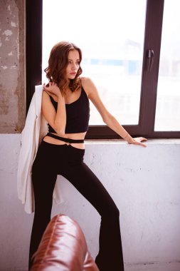 Evin penceresinin yanında ceketli moda bir kadın var.