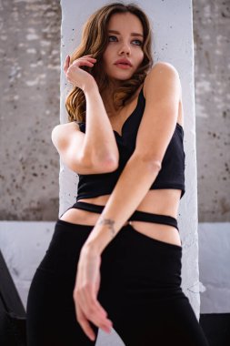 Evdeki duvarın yanında siyah elbiseli modaya uygun bir kadının düşük açılı görüntüsü