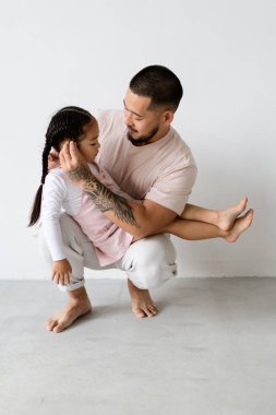 Çıplak ayaklı genç Asyalı baba gri arka planda kızının saçlarını düzeltiyor.