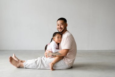 Gülümseyen Asyalı bir baba bebeğe sarılıyor ve gri arka plandaki kameraya bakıyor.