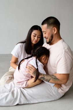 Gülümseyen dövmeli Asyalı adam gri arka planda küçük kızıyla oynuyordu.