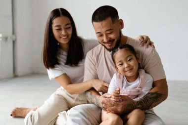 Gülümseyen Asyalı baba, gri arka planda küçük kızına sarılıyor.