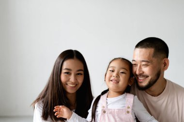 Küçük kızıyla birlikte gri arka planda kameraya bakan Asyalı bir ailenin portresi.