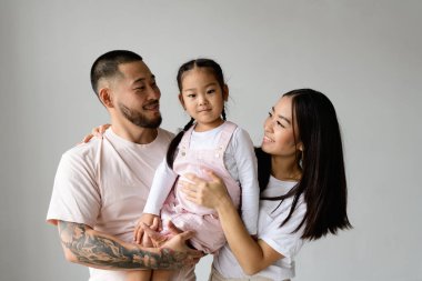Genç, modern Asyalı ebeveynler gülümsüyor ve kucağında küçük bir kız çocuğu var.