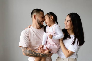 Mutlu Asyalı anne-babalar, gri alanda küçük kızı bir arada tutuyorlar.